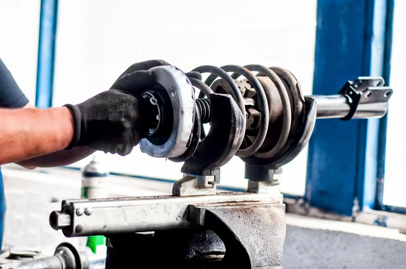 Gloved hands fitting a coil spring onto a shock absorber strut held in a spring compressor