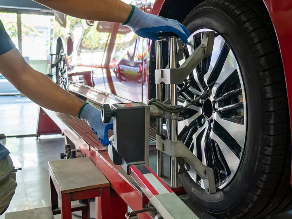 Mechanic in blue gloves attaching a wheel alignment clamp to a car's alloy wheel
