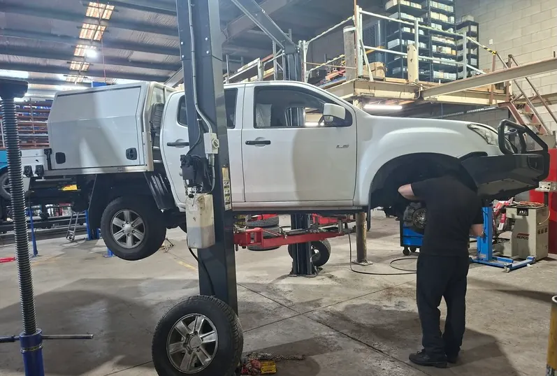 Technician working on the front wheel of a white ute raised on a hoist in the SA Suspension workshop